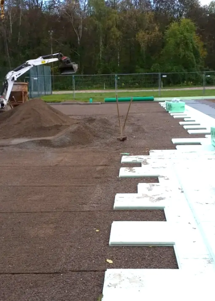 Bauarbeiter neben Minibagger auf Baustelle mit aufgeschüttetem Erdwall und verlegten Dämmplatten auf dem Boden
