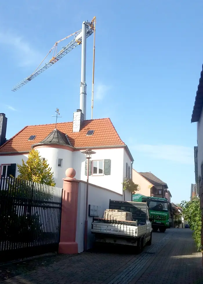 Neubau mit Baukran hinter einem historischen Wohnhaus mit rotem Ziegeldach an einer schmalen Straße